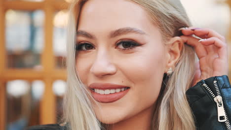 retrato de una joven rubia maquillada con labios pintados y manicura mirando a la cámara