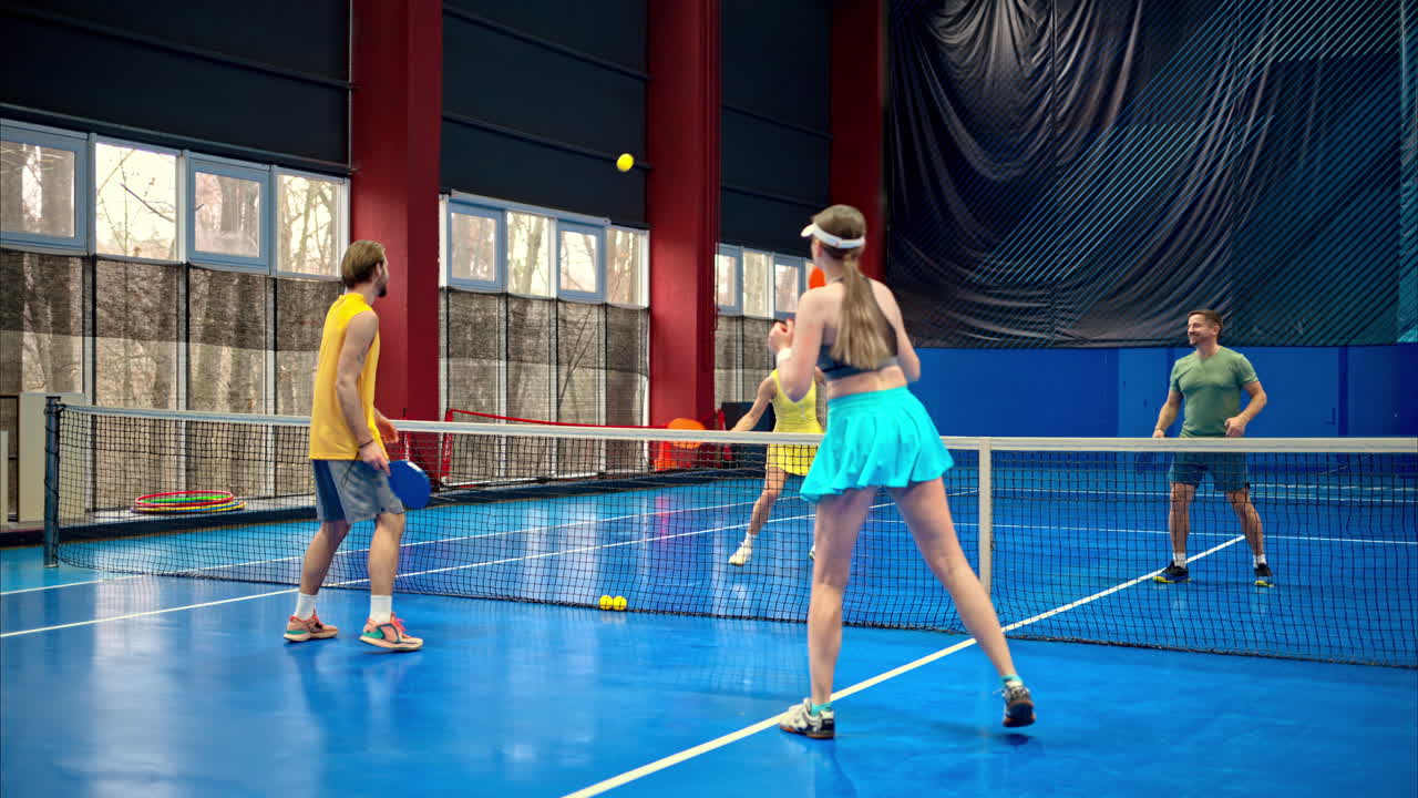 Two men and two women playing pickleball on a blue, inside court