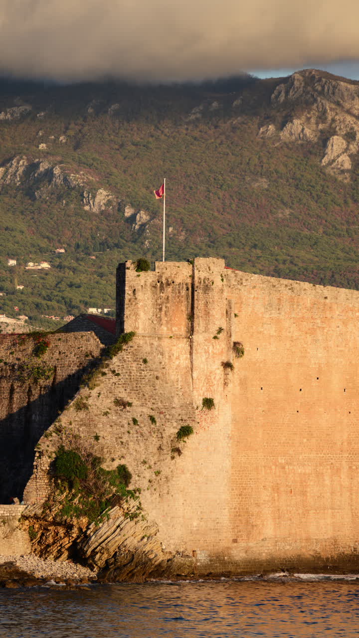 Mura della cittadella della Città Vecchia di Budva e torre campanaria che si affacciano sul Mare Adriatico, con montagne sullo sfondo