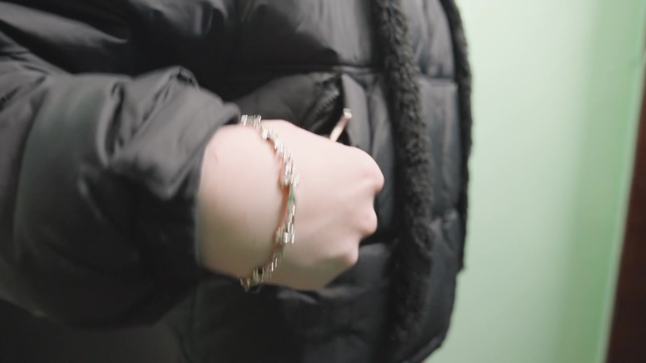 Closeup white woman hands holding keys against black puffer jacket, slow fumbling motion to unlock metal door, visible bracelet and keyring, tense body language in narrow corridor, realistic urban