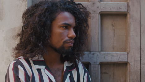 close up on mysteriously looking arabic black man sits under a giant wooden door of an old house