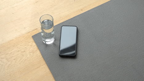 smartphone and glass of water resting on gray yoga mat at home, copy space