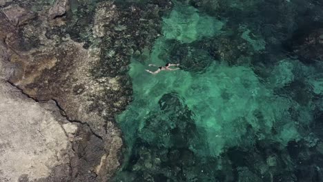 vista superior de una niña saltando al mar turquesa claro entre rocas