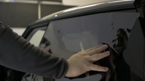 man fits car window tinting foil and cuts to size using knife