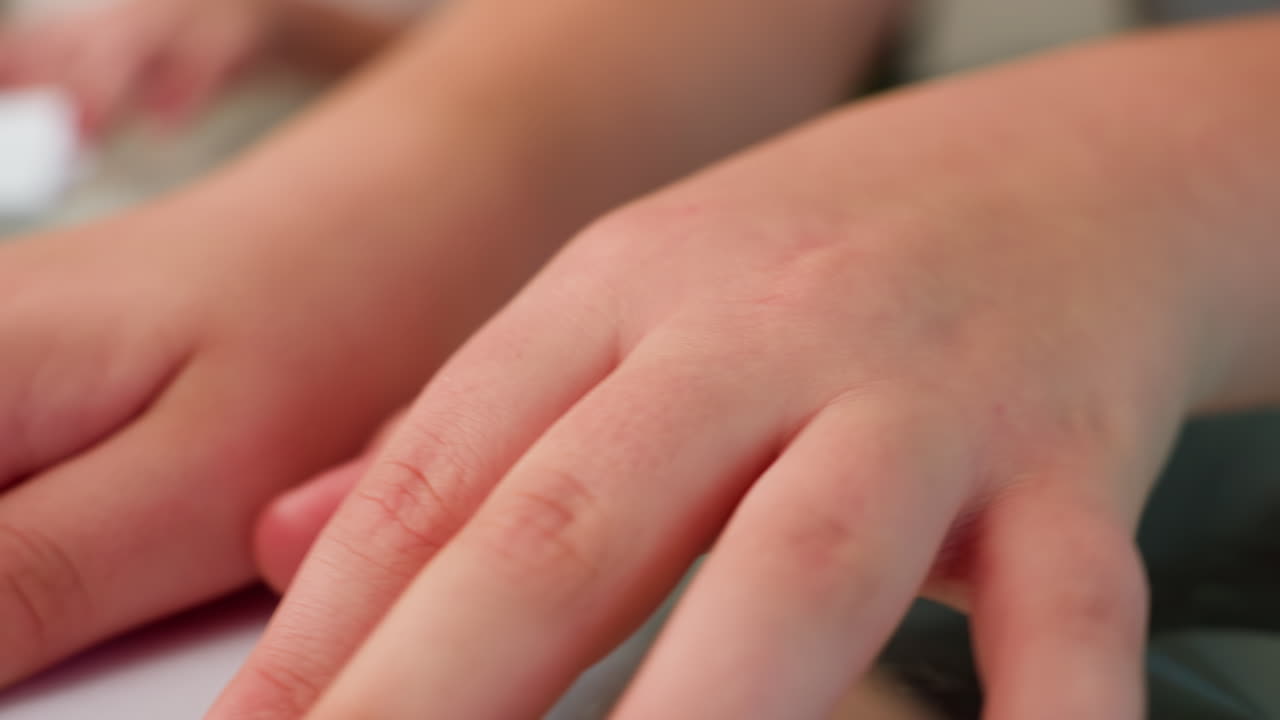 Close-up hand view of child working on paper craft, carefully folding and arranging paper on a glass table, showcasing focused hands-on activity and attention to detail