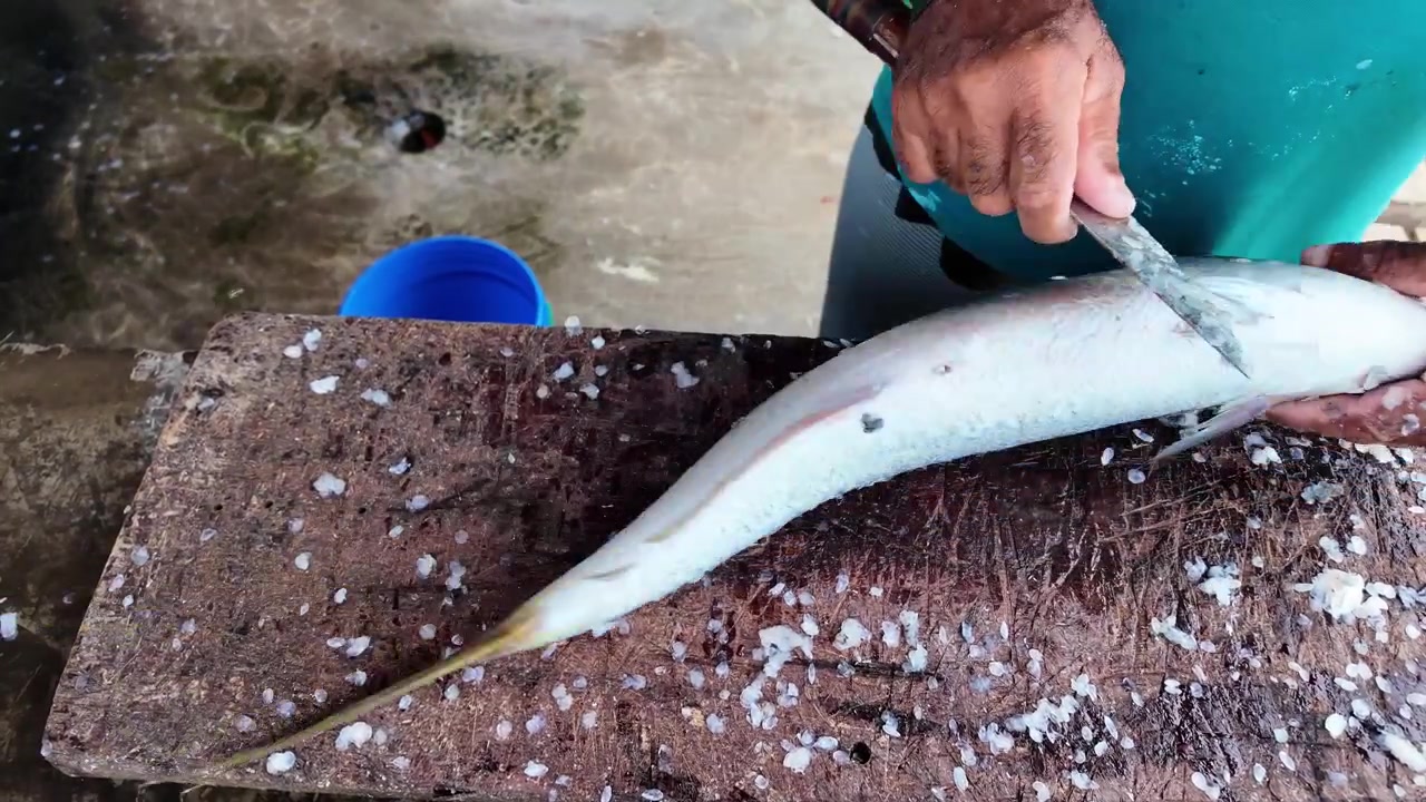 Hands scaling a fresh raw fish on a rustic wooden table at a fish cleaning station