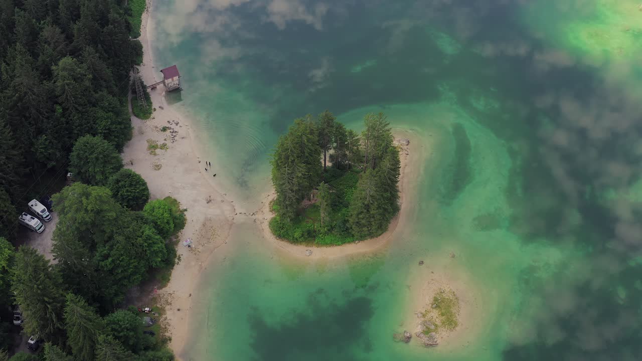 toma aérea - pequeña isla verde en el lago alpino, reflejo del cielo en agua verde esmeralda clara, campistas, dos perros corriendo
