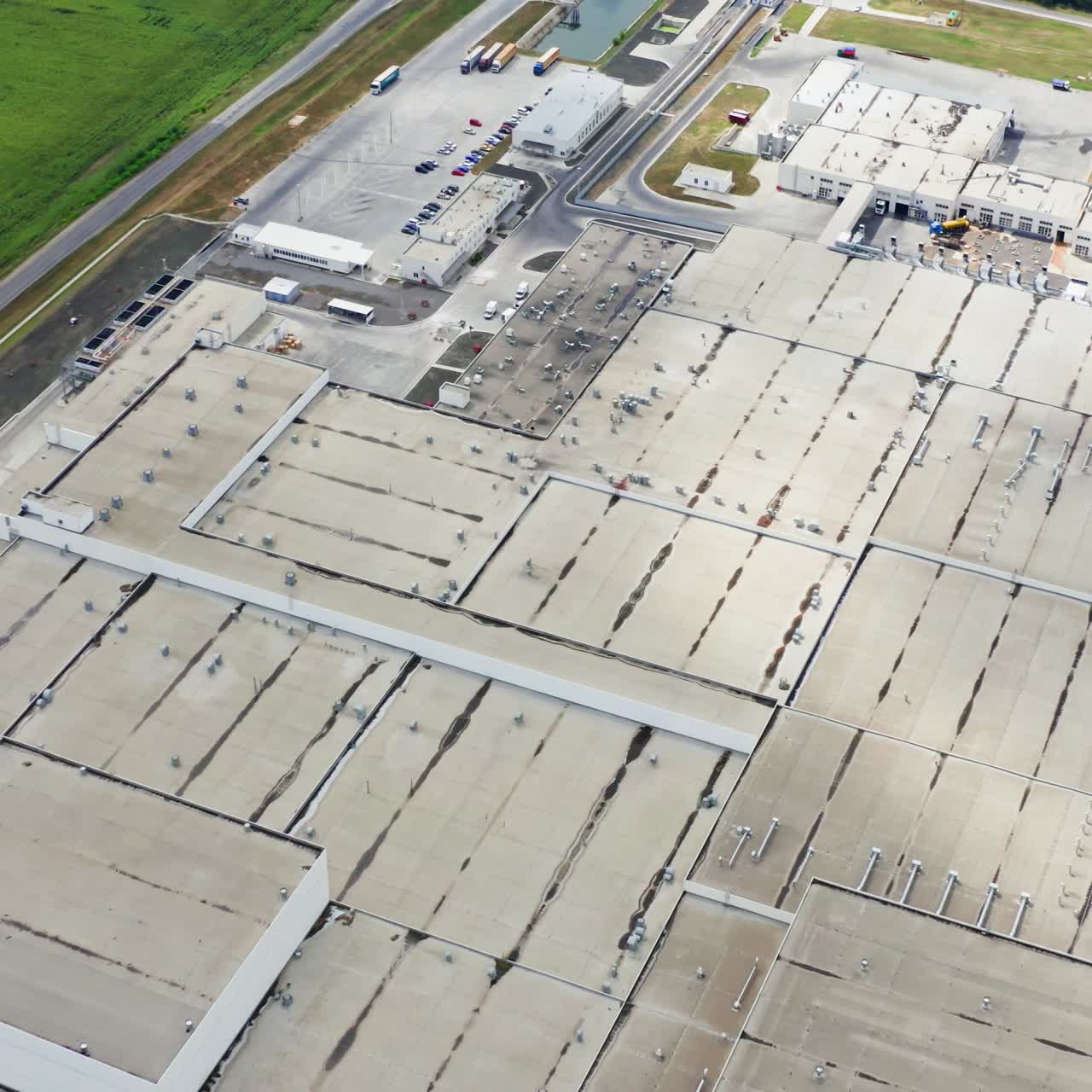 Rooftop of a big factory on field. Flight over industrial complex. Large manufacturing near green field. Aerial view