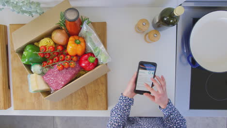 overhead shot of woman in kitchen with fresh ingredients looking at online recipe on mobile phone - shot in slow motion