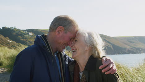 loving active senior couple hugging as they walk along coastal path together