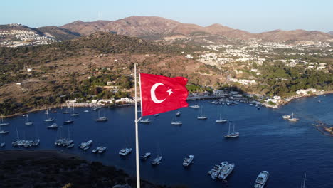 Bandera-Turca-Con-Vistas-Al-Paisaje-Marino-Y-Montañoso-En-Gumusluk,-Bodrum,-Pavo