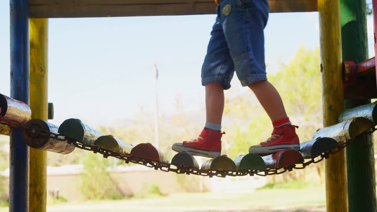 niño subiendo a un pequeño puente colgante de madera en el patio de recreo 4k