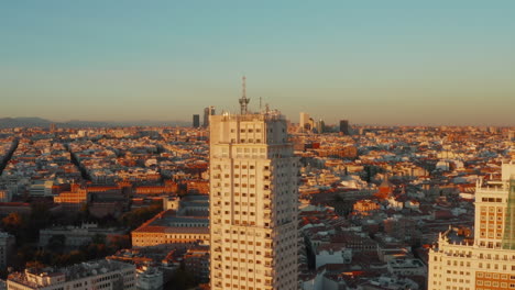 Erhöhte-Aufnahme-Der-Stadtentwicklung,-Die-Von-Hellem-Sonnenuntergangslicht-Beleuchtet-Wird.-Torre-De-Madrid-Historisches-Hochhaus-Im-Vordergrund.