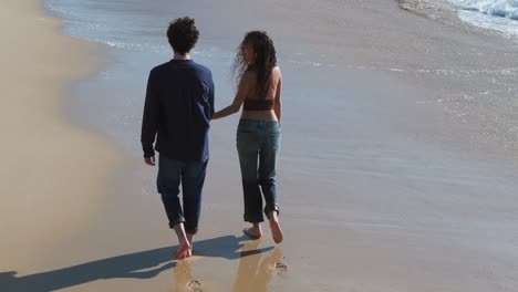 lovely couple strolling barefoot at the beach, holding and looking at each other with love and affection. high angle shot