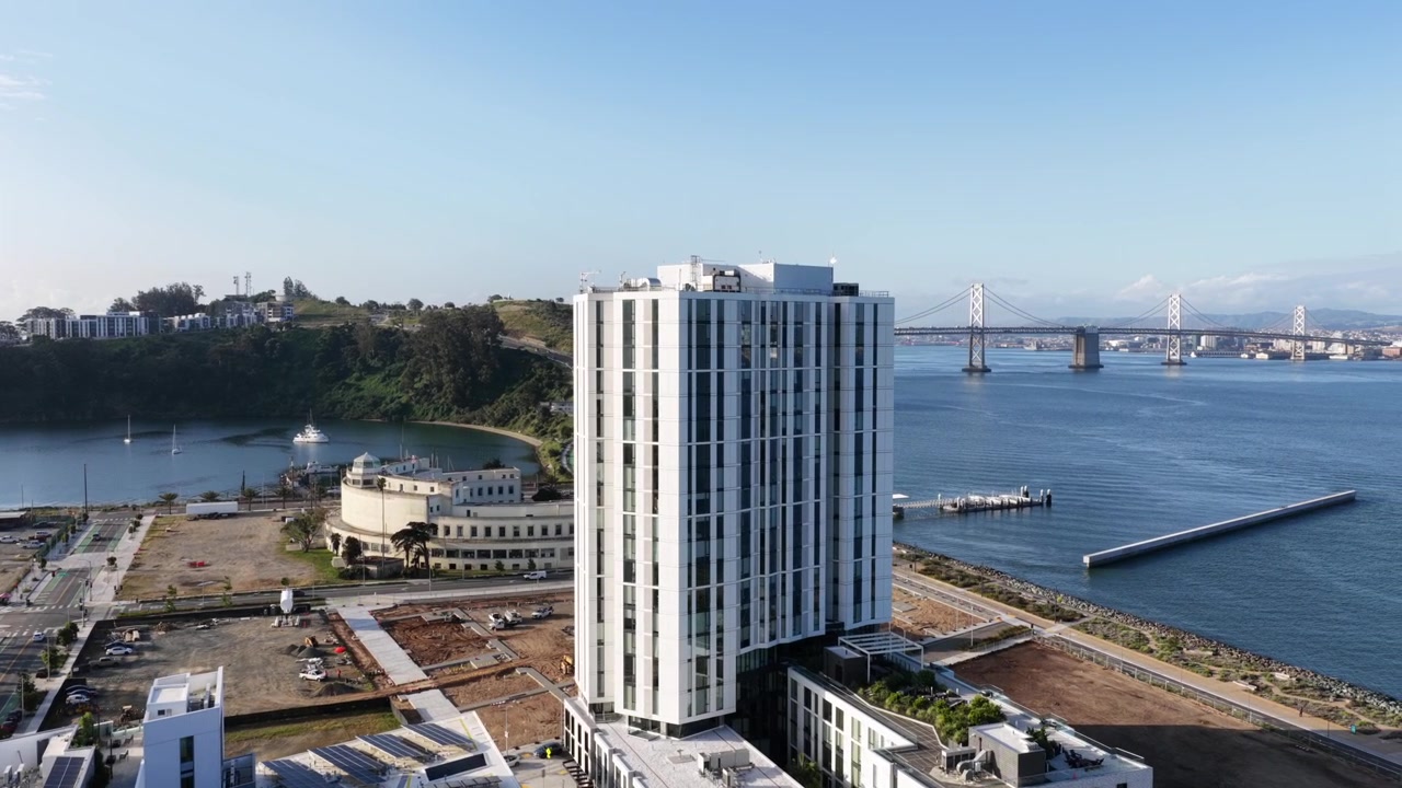 Edifício de apartamentos moderno na Ilha do Tesouro em São Francisco, Califórnia, EUA, com cenário à beira-mar, vistas da baía, ponte próxima e arquitetura residencial limpa em paisagem urbana costeira. Aéreo.