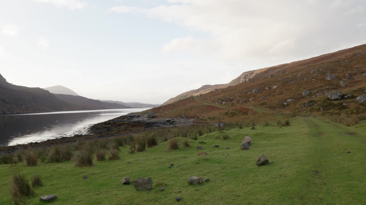 느린 왼쪽 팬은 가파른 절벽, 산, 시골 스코틀랜드의 외딴 글렌에 있는 바다 호수 사이에 있는 오래된 석조 건물을 보여줍니다.