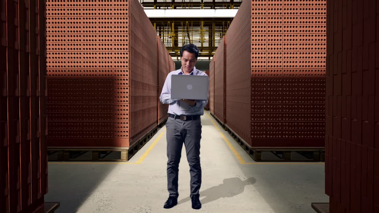Full Body Of An Asian Male Professional Worker Standing With His Laptop With Red Brick Packed in Stacks Are Stored, Working Continuously
