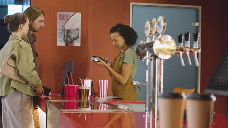 smiling female clerk selling movie tickets to a couple and the woman paying with phone 1