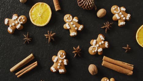 video of smiling gingerbread men and spices, slices of orange and nuts over black background