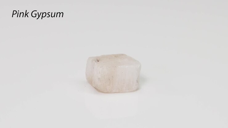 A pink gypsum crystal rotating on white surface