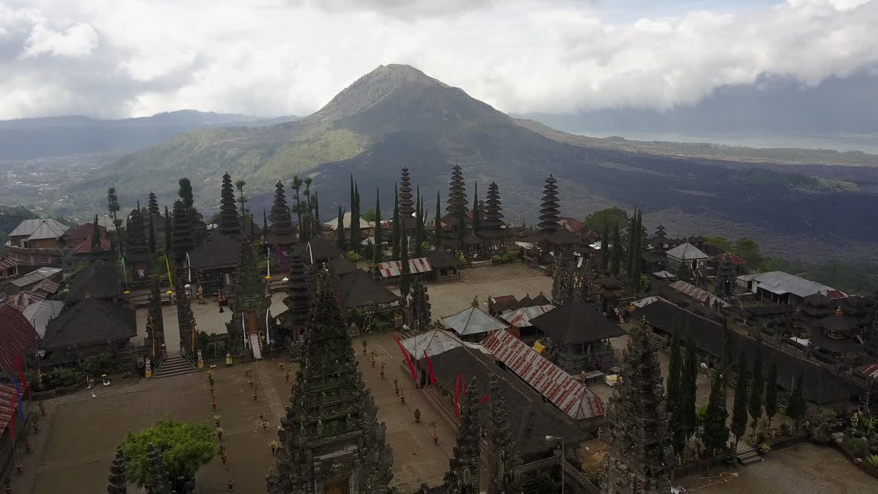 Rekaman drone udara yang menunjukkan orbit lateral lambat mengelilingi Pura Besakih sambil menjaga kompleks tetap terpusat, dengan gunung berapi Gunung Agung di latar belakang, menangkap arsitektur tradisional dan kehidupan sehari-hari.