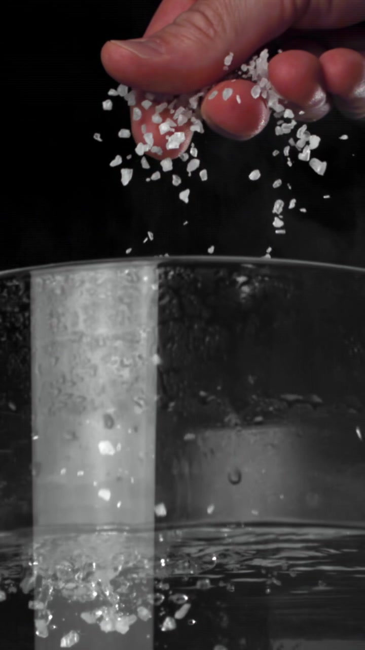 Hånd drysser groft salt i kogende vand i slowmotion