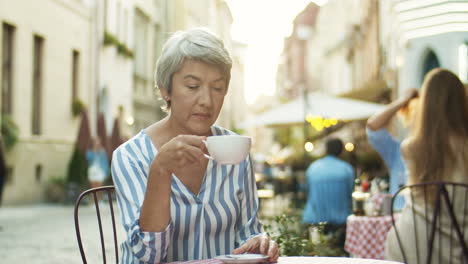 Schöne-Seniorin-Mit-Kurzen-Grauen-Haaren,-Die-Draußen-Am-Tisch-Im-Café-Ruht