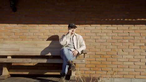 caucasian man talking on the phone while sitting on a bench outside a country house