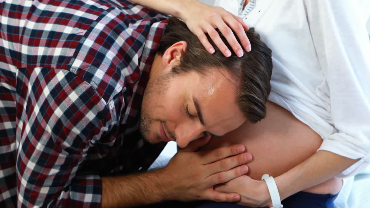 미소 짓는 남자 가 임산부 의 배 를 듣고 있다