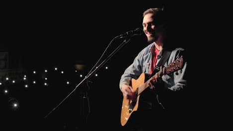 a musician is playing guitar on a large stage with audience members holding flashlights in the background. the auditorium is filled with beautiful flashing lights.