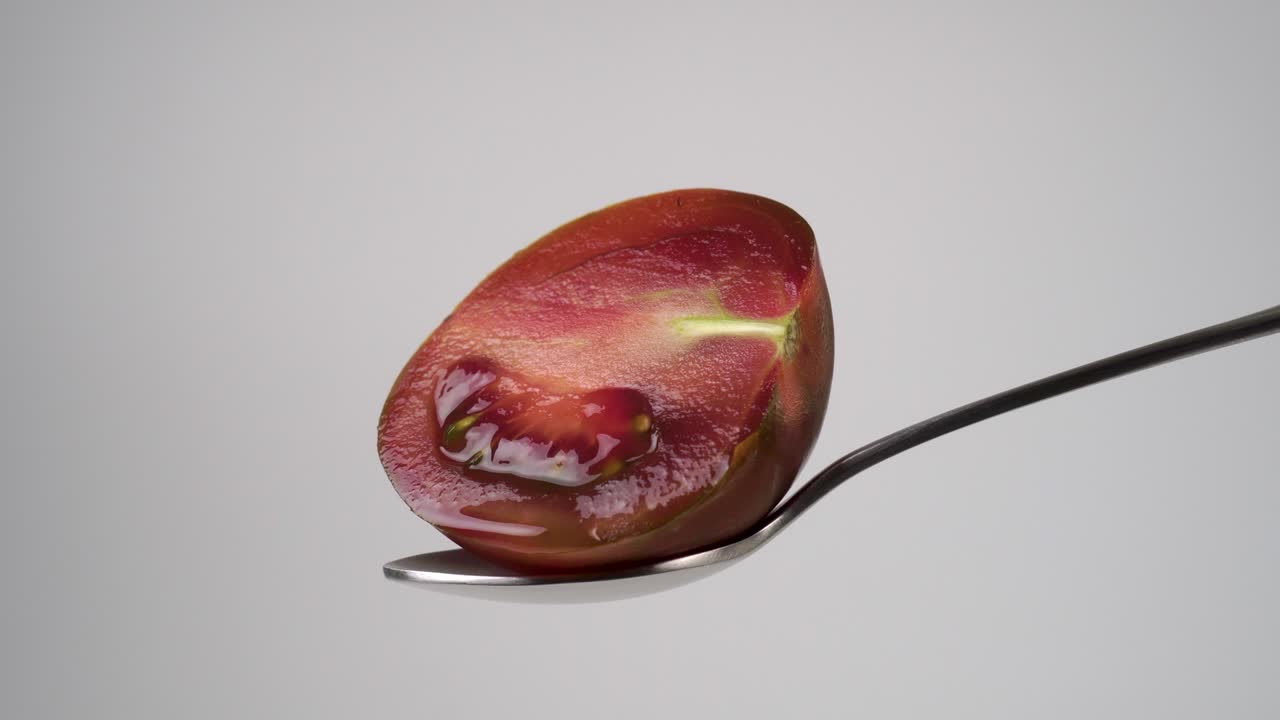 Wet juicy ripe brown kumato tomato sliced in half on a teaspoon