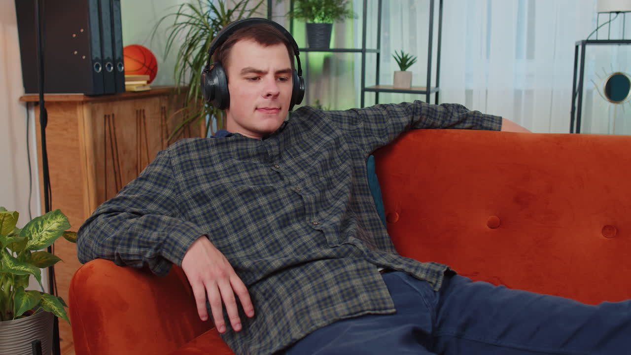 Uomo felice e rilassato con le cuffie wireless che balla ascoltando la sua musica rock n roll preferita sul divano di casa