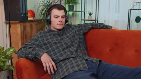 happy relaxed man in wireless headphones dancing listening favorite rock n roll music on home couch