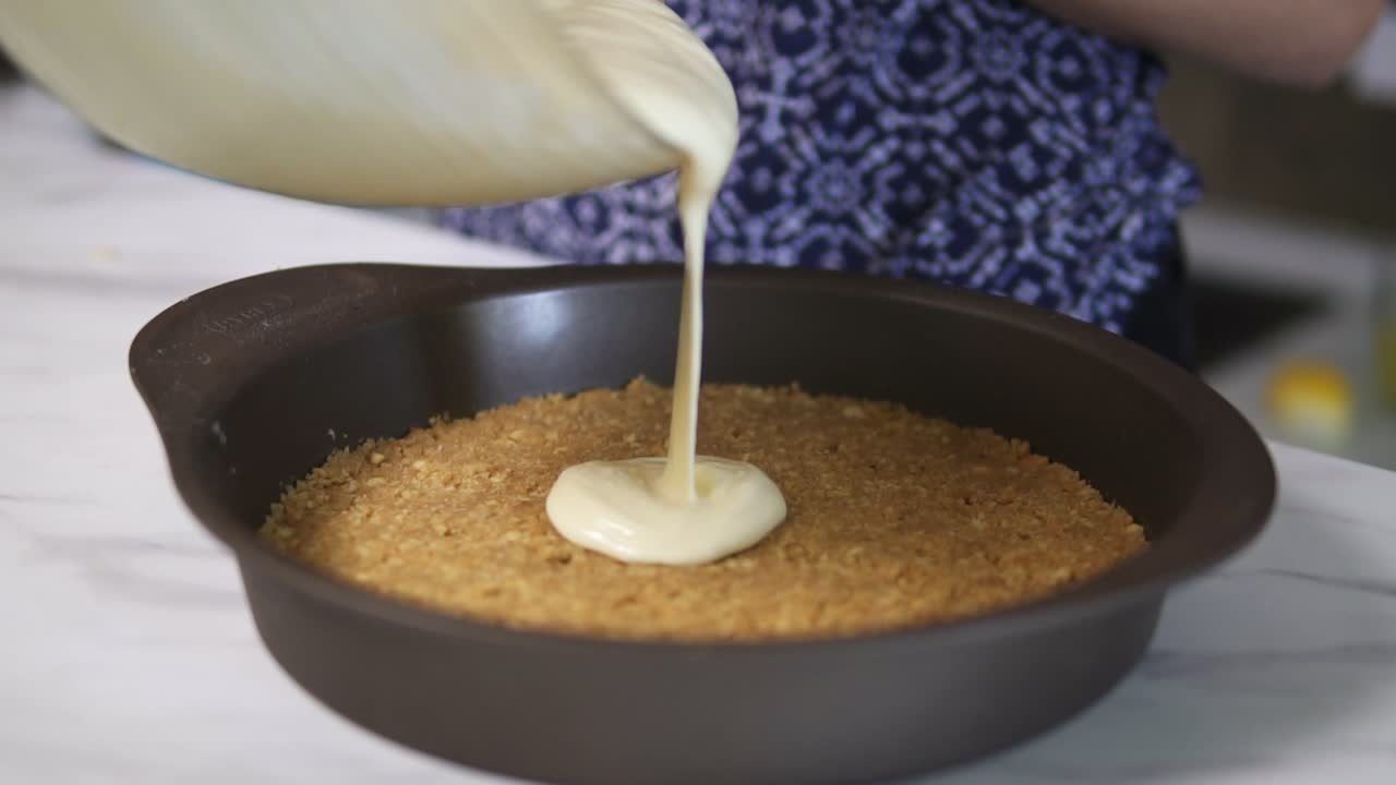 cubierta de queso de crema blanca extendida en la base de una galleta durante la preparación del pastel de queso. panadería casera. toma en cámara lenta