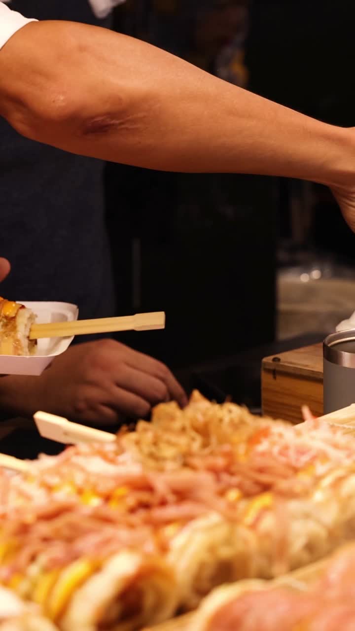 A vendor carefully places a freshly prepared rice roll into a container at a market