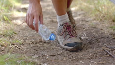 una persona recoge una botella de plástico mientras camina por un camino de tierra y recoge basura