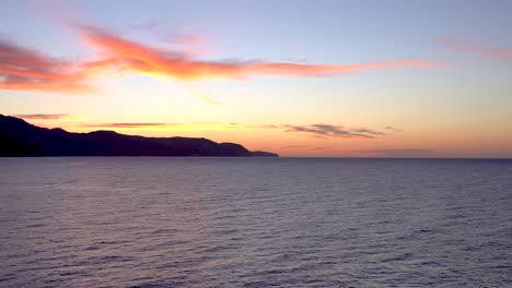 Slow-tilt-up-over-beautiful-ocean-sunrise-with-mountain-silhouette