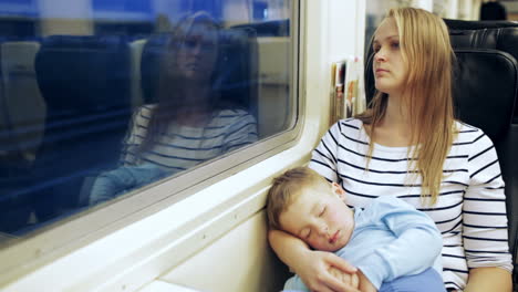 woman looking out the train window with her son sleeping on lap