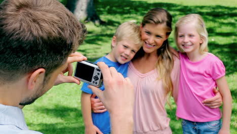 a man points a camera at his family who hold each other before they turn to the camera and smile