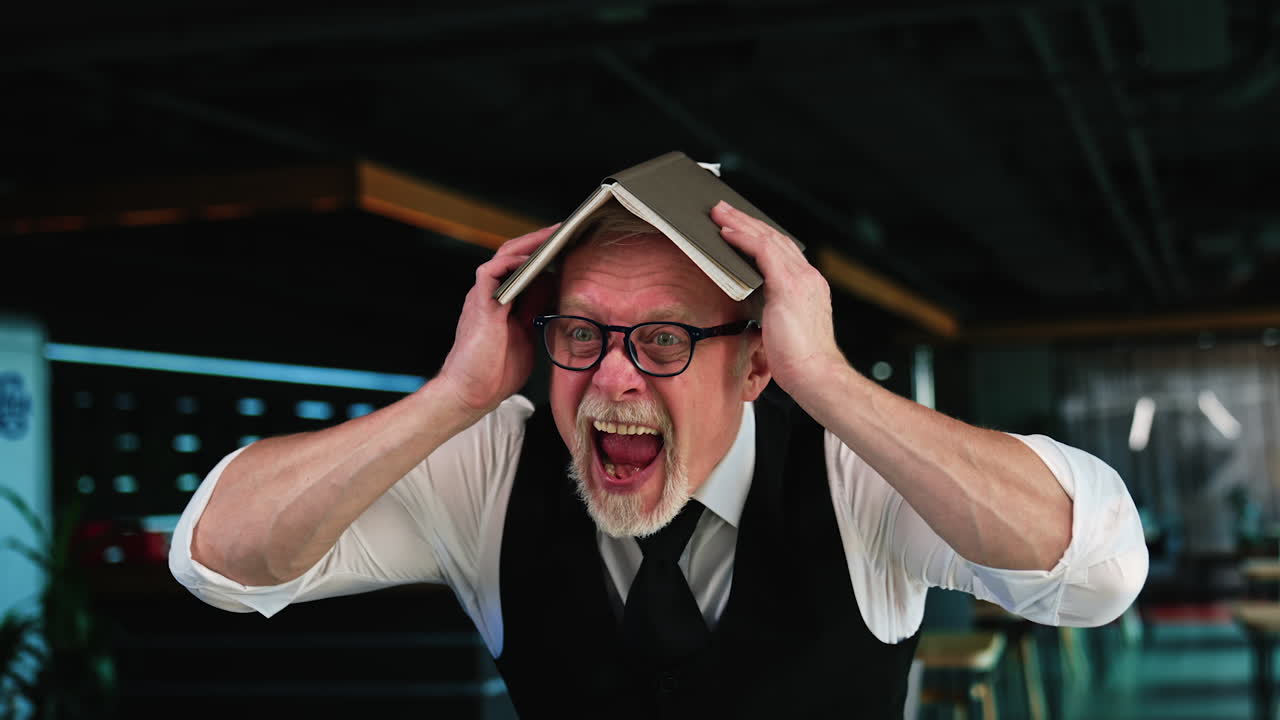 Businessman going crazy in office. Man holding a book on his head screams with a scary face.