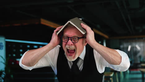 businessman going crazy in office. man holding a book on his head screams with a scary face.