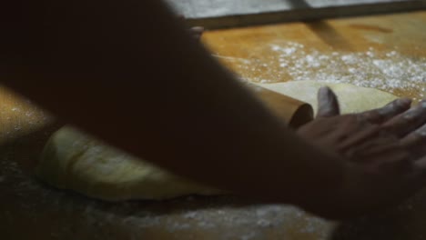 freshly raised dough pressed flat using rolling pin on wooden kitchen top by chef, filmed as close up slow motion shot