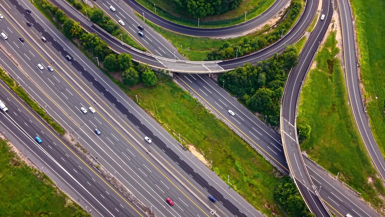 Aerial view of highway curve merging with exit ramp, New Jersey. Drone shot of overpass bridge, curved lanes and forest surrounding multilane roadway.