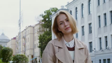 woman in beige trench coat, smiling in city