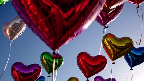 multiple heart shaped balloons in various colors, attached to strings, ascend gracefully against a clear blue sky, creating a vibrant and cheerful atmosphere