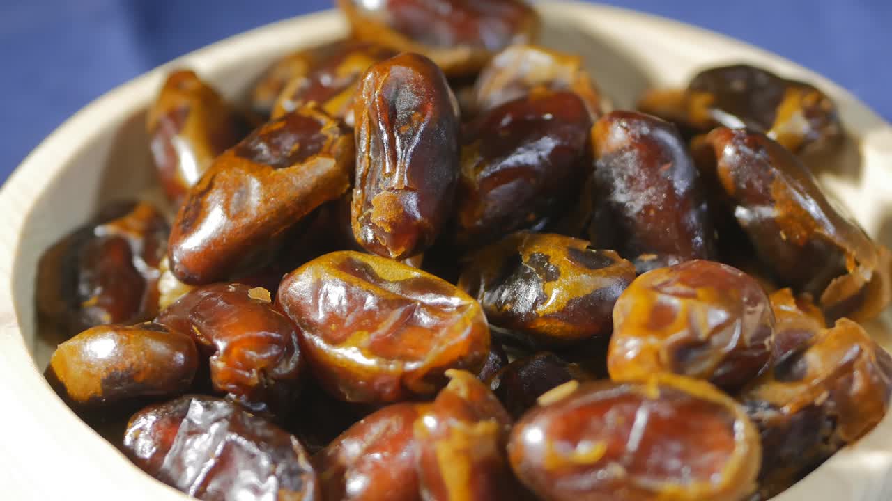 sweet arabic dates. Close-up of dates lying in a white plate made of wood. On a blue background. Fruits rotating in a circle. Backlit with warm light. healthly food. eco products
