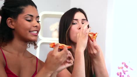 cute women enjoying pizza sitting on couch