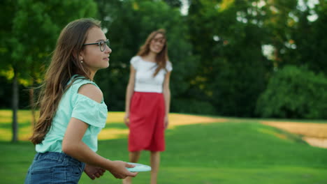 woman throwing frisbee disk to daughter in park. girl catching frisbee plate