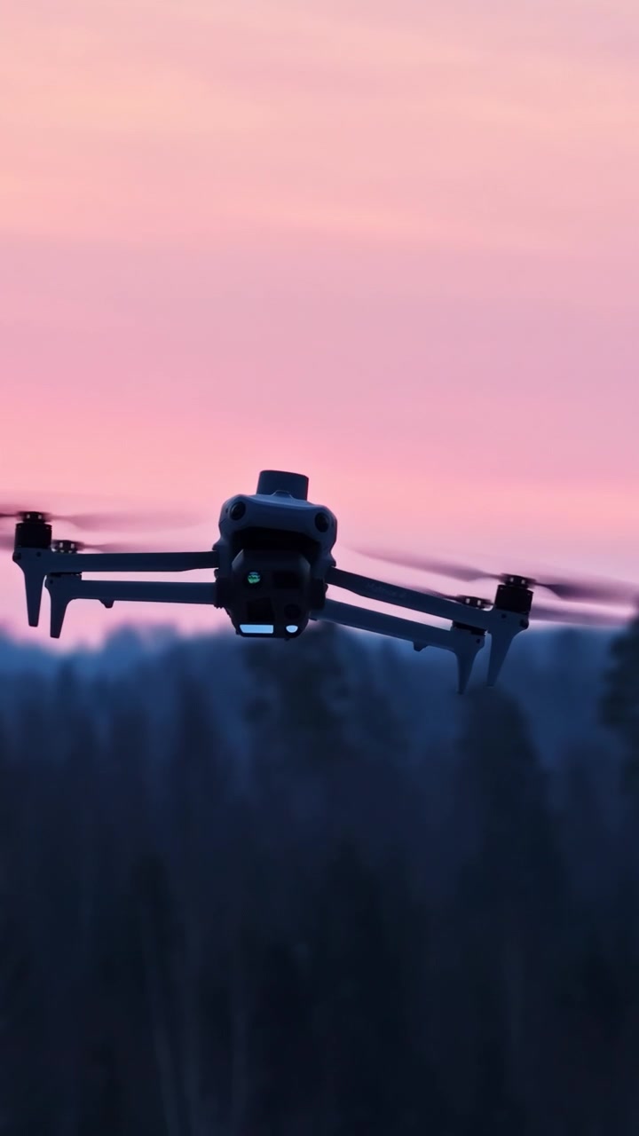 Dronesilhuet svæver og flyver i luften under en smuk og farverig solnedgang.