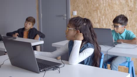 Pensive girl in glasses sitting at desk with laptop